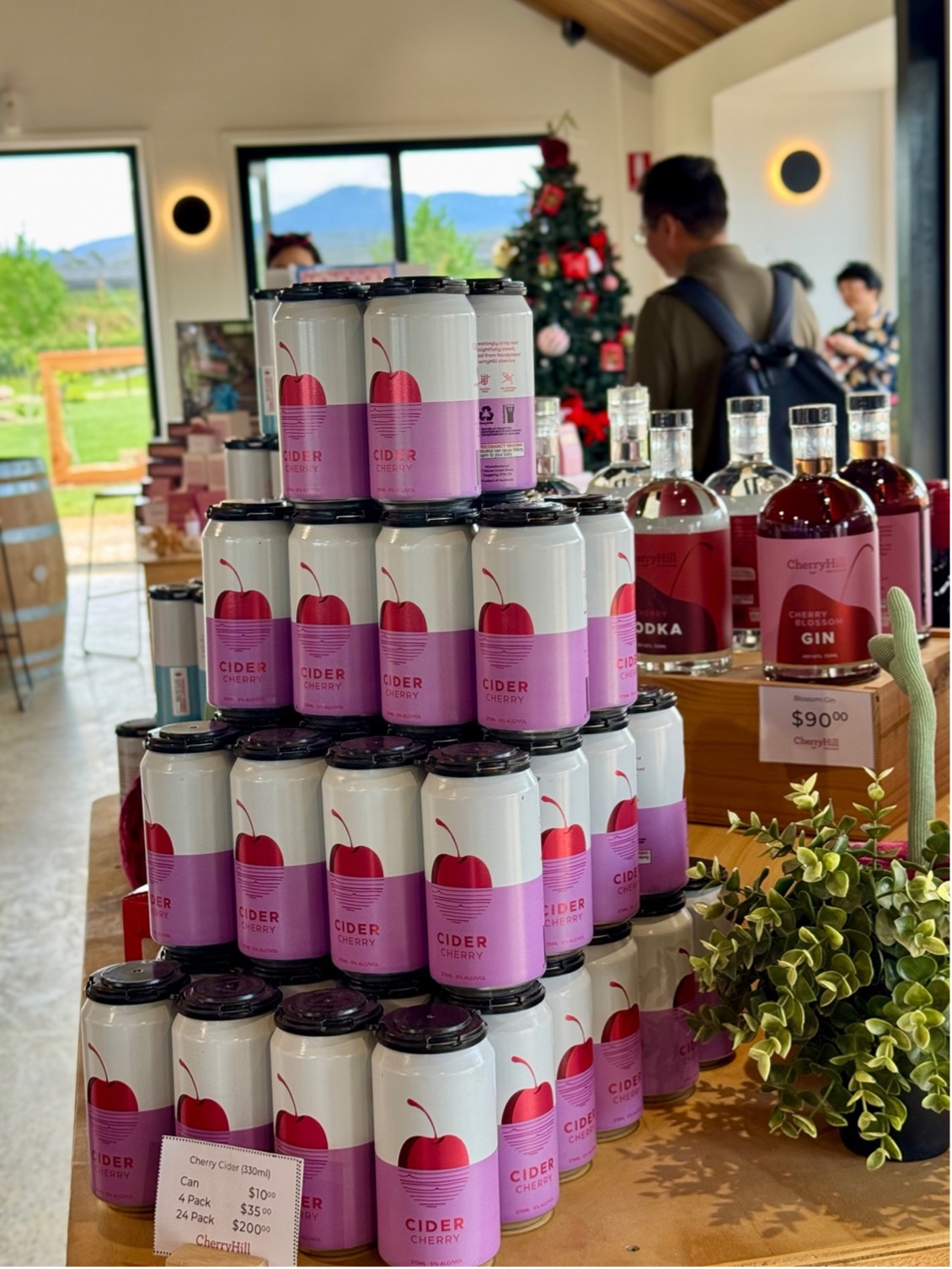 Cans of cherry cider stacked at the CherryHill Orchards farmgate store with spirits and a Christmas tree in the background