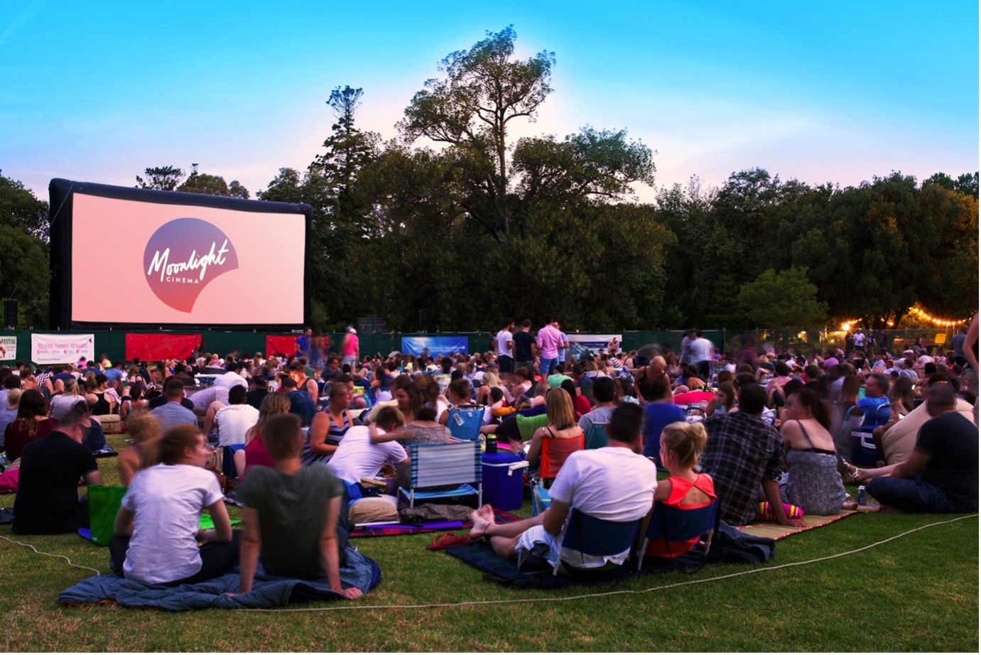 Crowd relaxing on picnic blankets at Moonlight Cinema in Melbourne’s Royal Botanic Gardens during sunset.