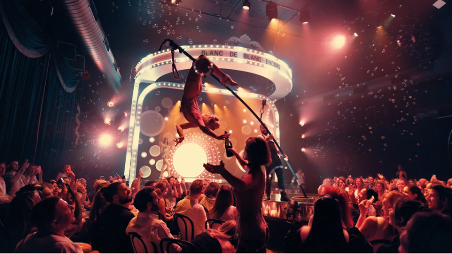 Aerial performer pouring champagne over the audience during Blanc de Blanc Encore at Spiegel Haus Melbourne, surrounded by bubbles and glowing stage lights.