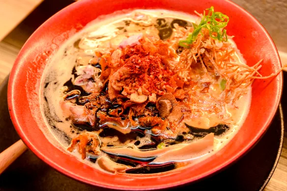 Shoyu ramen bowl with chashu pork, corn kernels, and dark, complex broth on a wooden table.
