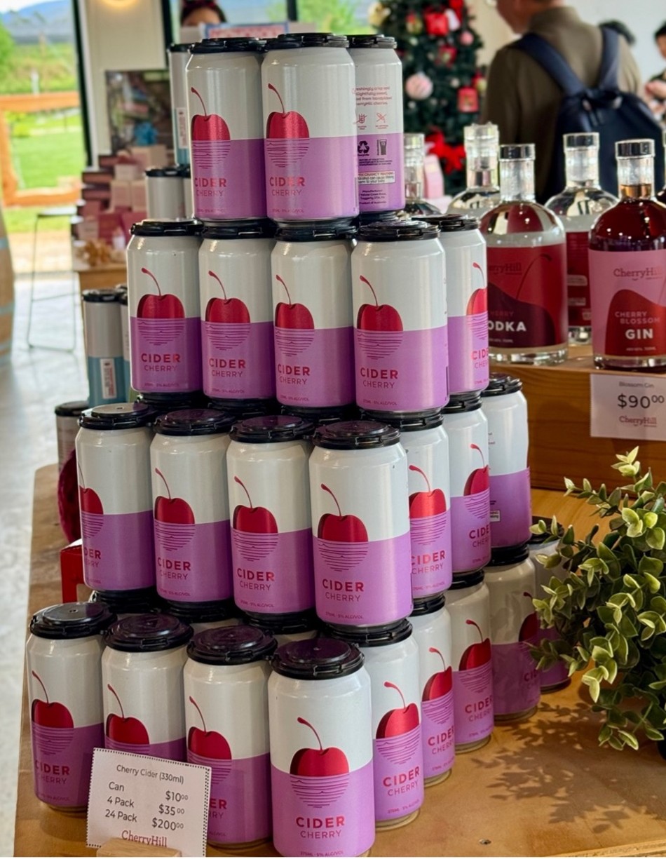 Cans of cherry cider stacked at the CherryHill Orchards farmgate store with spirits and a Christmas tree in the background