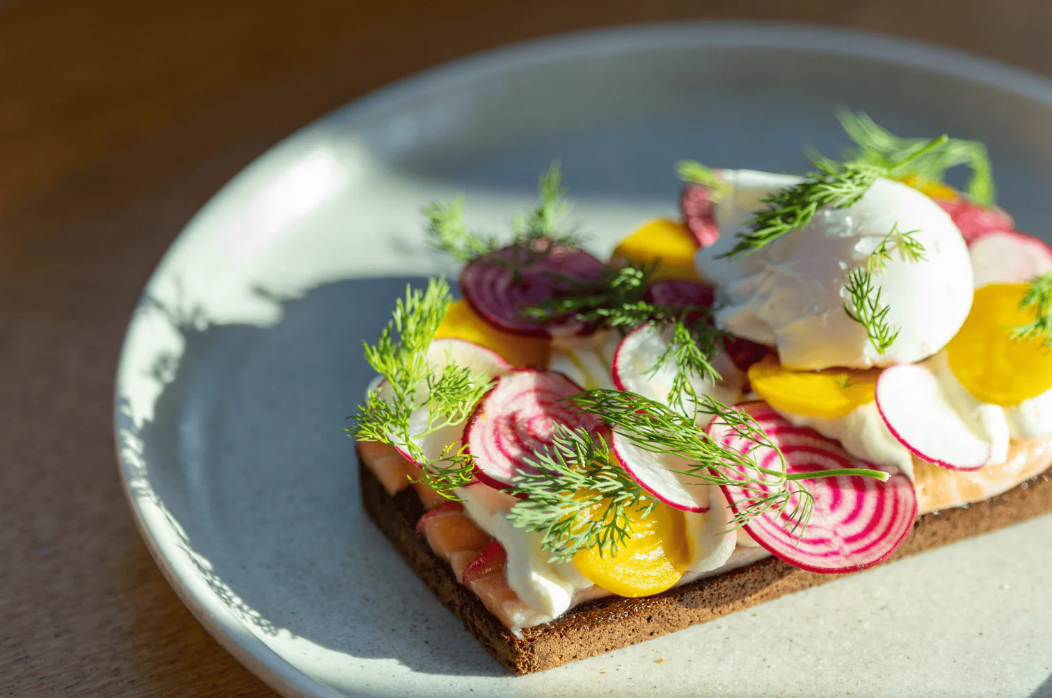 Open-faced rye bread topped with cream cheese, pickled radish, golden beetroot and poached egg at a Melbourne brunch cafe