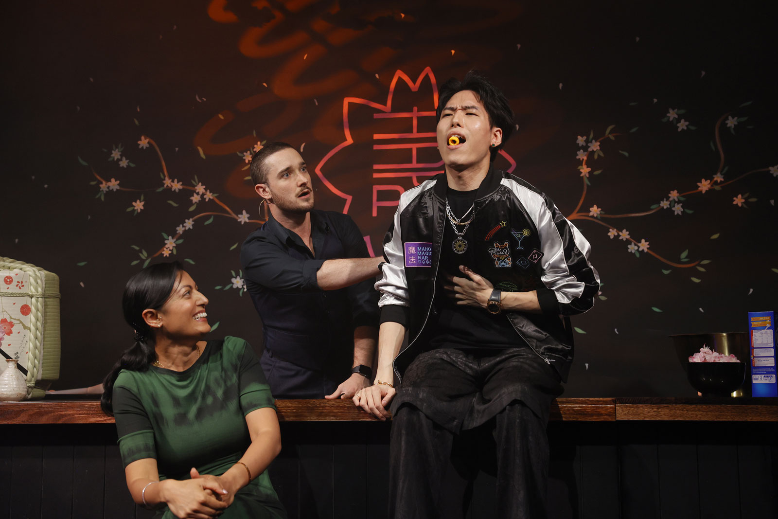 A costumed magician performs close-up card magic for delighted guests at a table inside Maho Magic Bar.