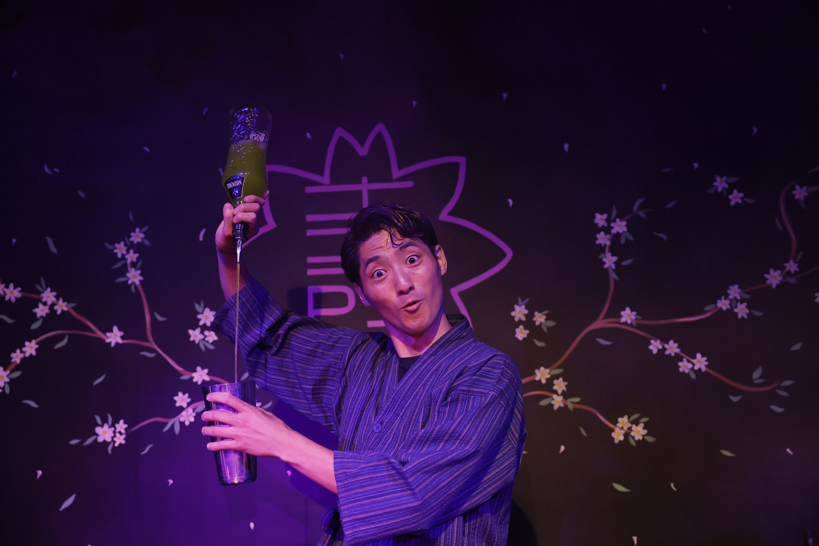 An entertaining bartender in a traditional Japanese kimono pours a green cocktail at Maho Magic Bar.