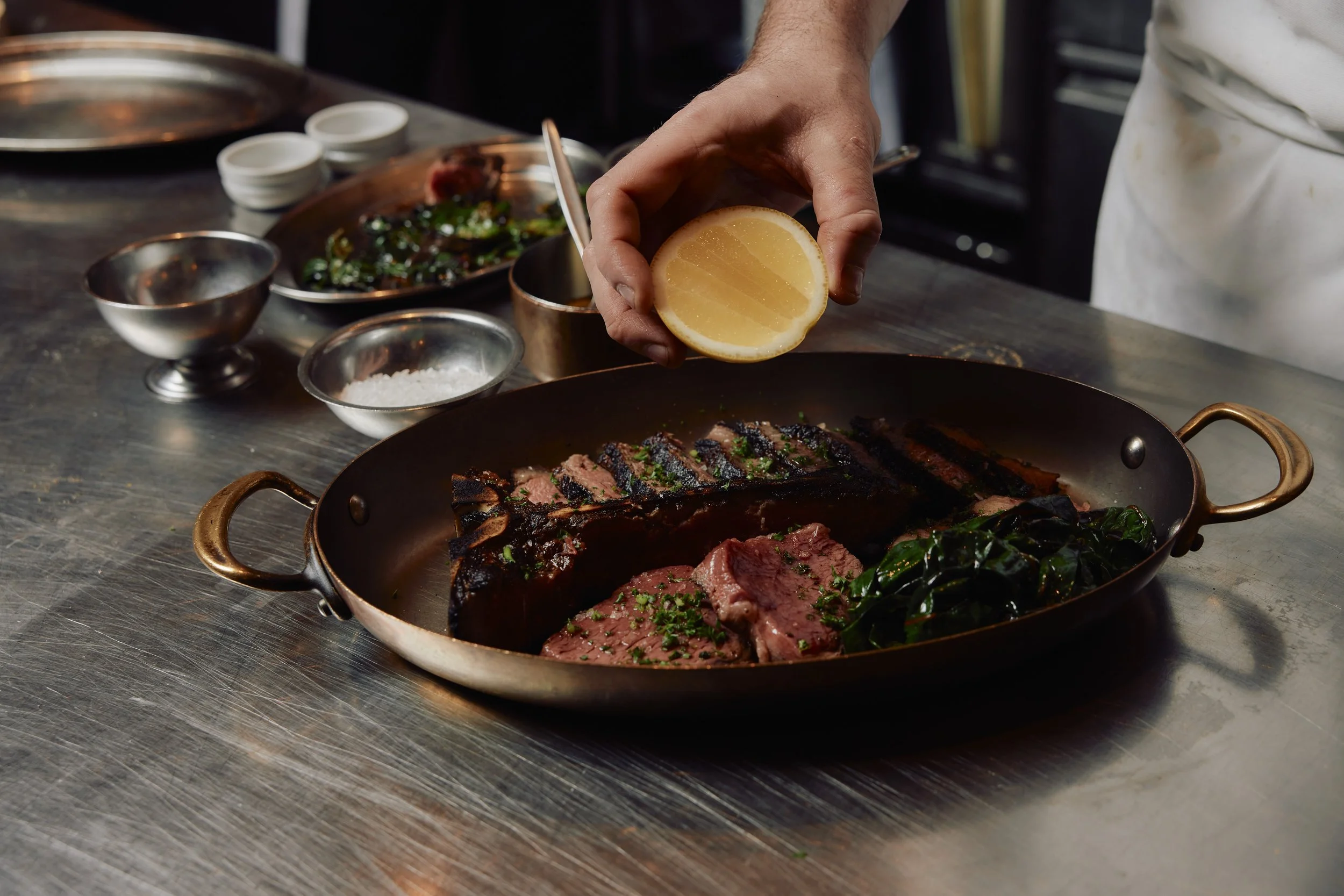 Wood fired steak Melbourne — chef finishing grilled beef in a copper pan with lemon at Gimlet at Cavendish House