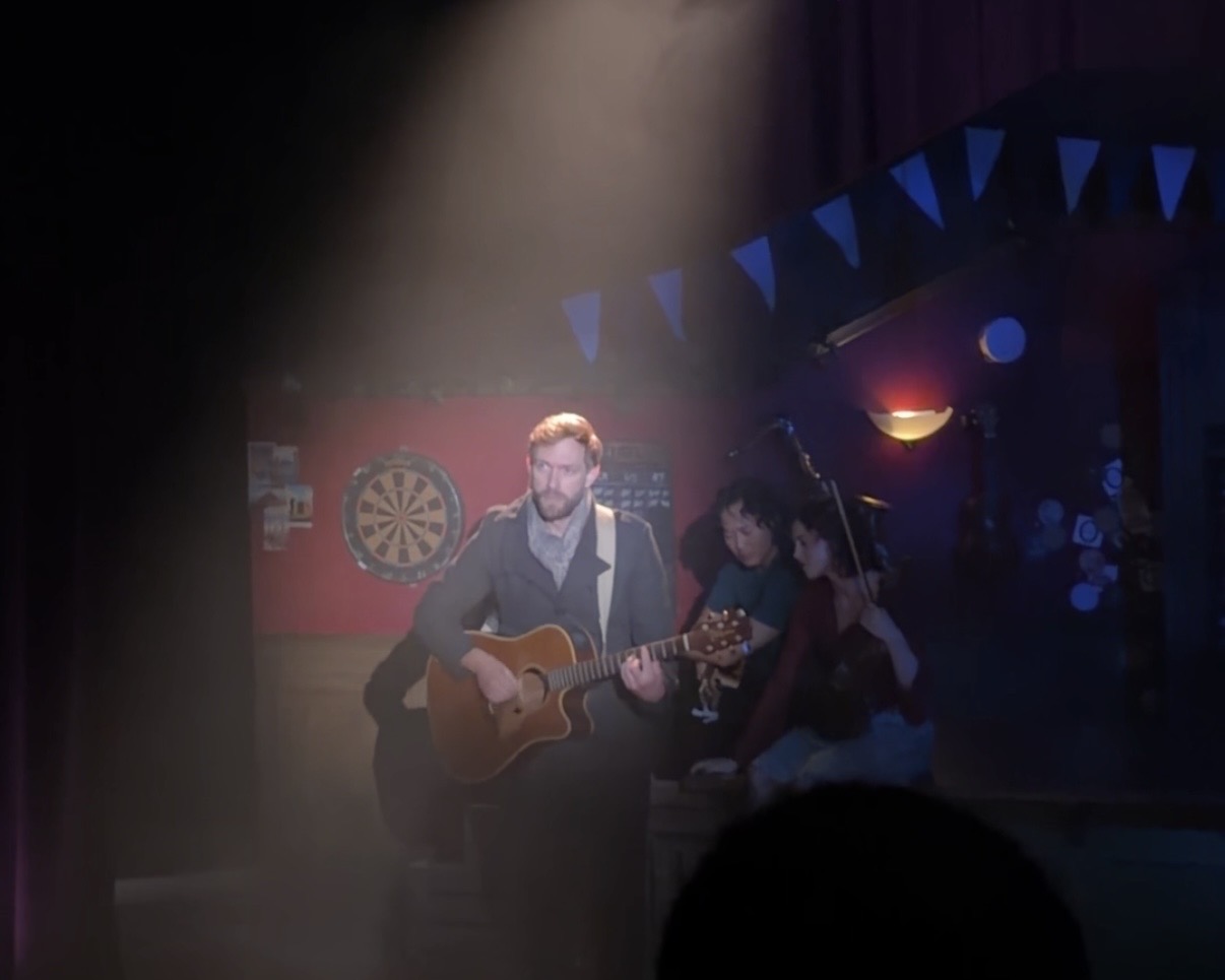 Mark Taylor as Guy performing solo with acoustic guitar under spotlight in Once the Musical Melbourne 2026 at Chapel off Chapel